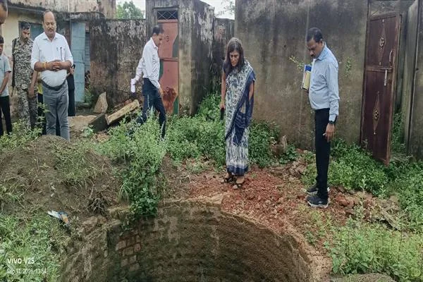 ईंटों से घिरे खुले कुएं के पास खड़ी महिला अधिकारी और निरीक्षण करते अन्य अधिकारी